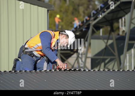 Ein Bauarbeiter, der einen Sicherheitsgurt trägt und in der Höhe auf einem Dach arbeitet Stockfoto