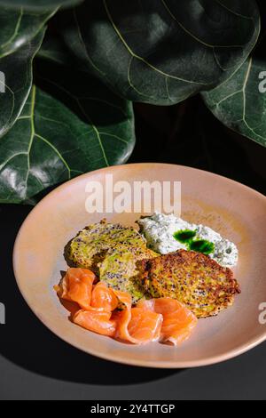 Zucchini-Krapfen mit Lachs und Frischkäse auf Keramikplatte unter grünen Blättern Stockfoto