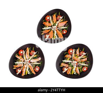 Drei Salate auf schwarzen ovalen Tellern mit Lachs, Garnelen, Avocado und Salat, wunderschön angeordnet und von oben auf weißem Hintergrund geschossen Stockfoto