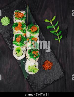 Sushi-Brötchen mit rotem Kaviar und Wasabi, serviert auf schwarzem Steinteller auf dunklem Holztischhintergrund Stockfoto