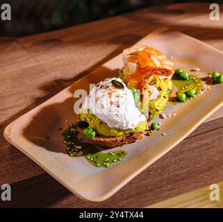 Zwei Scheiben Avocadotoast, eine mit Garnelen und eine mit einem pochierten Ei, liegen auf einem Teller mit grüner Garnitur Stockfoto