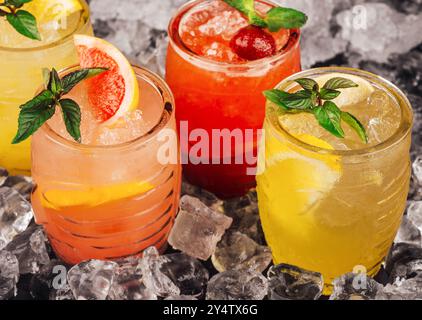 Vier farbenfrohe Sommercocktails ruhen auf Eis mit frischem Obst und Minzgarnitur Stockfoto