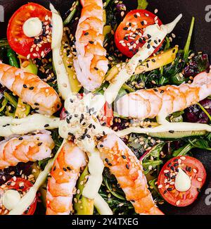 Frisch zubereiteter Salat mit Garnelen, Tomaten, Avocado und Sauce Dressing, serviert in einer schwarzen Schüssel Stockfoto