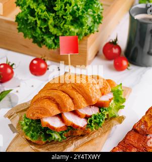 Frisch zubereitetes Croissant mit Schinken und Salat auf einem Holzbrett serviert Stockfoto