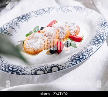 Hüttenkäsepfannkuchen mit Puderzucker, Erdbeeren, Heidelbeeren und Minzblättern serviert auf weißem Teller mit blauem Blumenmuster Stockfoto