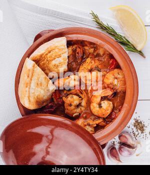 Köstlicher Eintopf mit Garnelen und Tomaten, serviert in Tontopf mit Brot und Zitrone Stockfoto