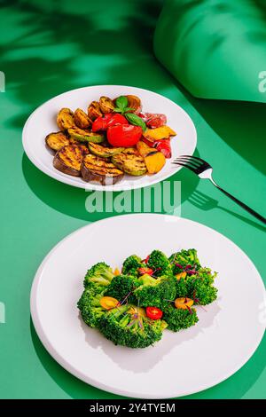 Zwei Teller sind mit gegrilltem Gemüse gefüllt und auf einem leuchtend grünen Hintergrund mit kontrastierenden Schatten angeordnet Stockfoto