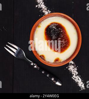 Türkischer Reispudding Sutlac wird in einer Schüssel aus Steingut auf schwarzem rustikalem Hintergrund serviert Stockfoto