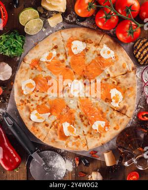 Köstliche Pizza mit Lachs, rotem Kaviar und Mozzarella auf Holztisch, umgeben von frischen Zutaten Stockfoto