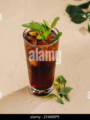 Auf einem Tisch steht ein hohes Glas mit einem erfrischenden dunklen Cocktail, der mit frischen Minzblättern dekoriert ist Stockfoto
