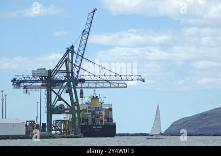 Lyttleton, Neuseeland, um 2014: Ein Segelboot passiert ein Containerschiff, das im Hafen von Lyttleton auf Südinsel, Ozeanien, entlädt Stockfoto
