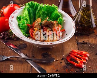 Die weiße Platte enthält eine Portion Rindereintopf aus Tomaten und Zwiebeln, garniert mit Salat Stockfoto