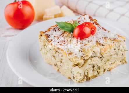 Eine Scheibe köstlicher vegetarischer Lasagne wird auf weißem Gericht serviert, mit frischen Zutaten garniert und kann genossen werden Stockfoto