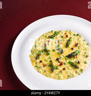 Cremiges Risotto mit Spargel und Pancetta, serviert auf einem weißen Teller auf einem Holztisch Stockfoto