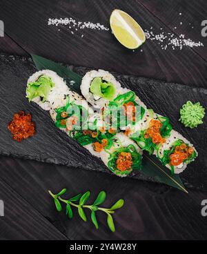 Sushi-Brötchen mit Kaviar, Algen, Reis und grünem Salat auf schwarzem Steinteller Stockfoto