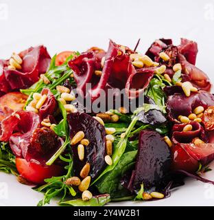 Frischer und gesunder Salat mit Schinken, Roter Bete, Rucola, Tomaten und Pinienkernen wird auf einem weißen Teller serviert Stockfoto