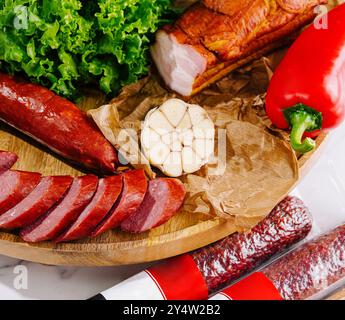 Auswahl an köstlichen Räucherwürsten mit Knoblauch und Salat auf Holzschneidebrett auf Marmortisch Stockfoto