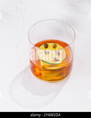 Erfrischender negroni-Cocktail wird mit einer Limettenscheibe und Kaffeebohnen garniert, serviert in einem Steinglas Stockfoto