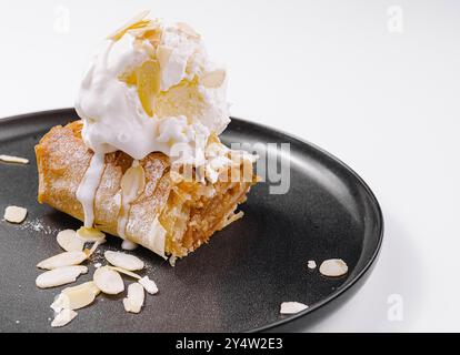 apfelstrudel mit Vanilleeis und Mandeln, serviert auf einem modernen schwarzen Teller Stockfoto