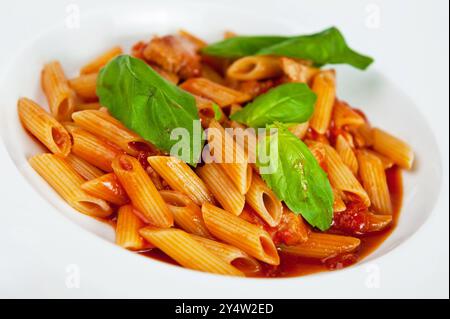 Köstliche Penne-Pasta in reichhaltiger Tomatensauce garniert mit frischen Basilikumblättern, serviert auf weißem Teller Stockfoto