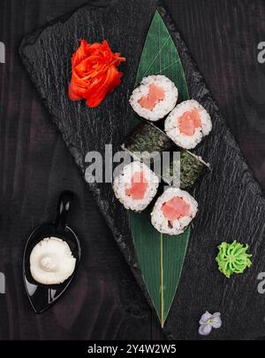 Köstliche Sushi-Brötchen mit Thunfisch auf schwarzem Steinteller, serviert mit Ingwer, Wasabi und Mayonnaise Stockfoto