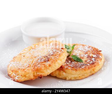 Zwei köstliche Hüttenkäse-Pfannkuchen mit Puderzucker, Sauerrahm und Minze auf weißem Teller Stockfoto