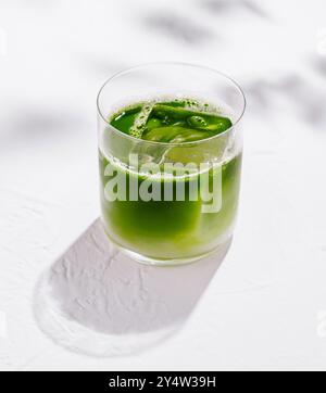 Erfrischende Eismatcha Latte sitzt auf einem weißen Tisch mit Schatten von Blättern im Hintergrund Stockfoto