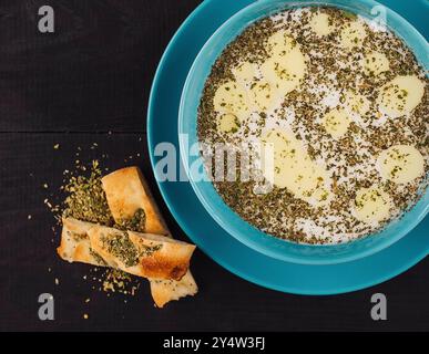 Türkische yayla-Suppe mit getrockneter Minze und geschmolzener Butter in blauer Schüssel auf rustikalem dunklen Holztisch, serviert mit Fladenbrot, Blick von oben Stockfoto