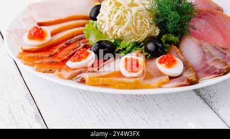 Auf einem weißen Holztisch wird eine in Scheiben geschnittene Fischplatte mit Butter, Zitrone und Oliven serviert Stockfoto