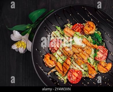 Köstlicher warmer Salat mit gegrilltem Huhn, Riesengarnelen und Sesamsamen auf schwarzem Teller Stockfoto