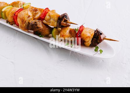 Aus nächster Nähe sehen Sie saftige Grillspieße mit Huhn, Pilzen, Paprika und Zucchini auf einem eleganten Gericht Stockfoto