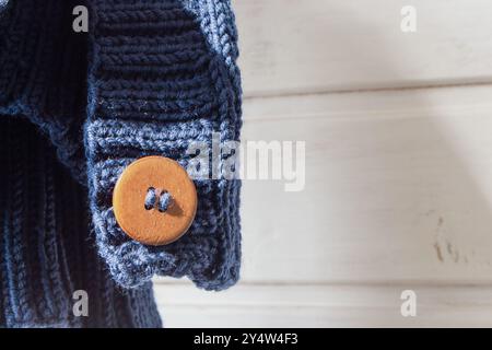 Blauer Strickpullover mit Holzknöpfen, Nahaufnahme. Strickjacke aus Wollgarn mit braunen Knöpfen bei Sonnenlicht. Bequeme warme Kleidung. Handgefertigtes Strickdesign Stockfoto