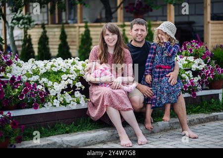 Die junge Familie entspannt sich in ihrem Garten und genießt die Sommerbrise mit ihrem neuen Baby und ihrem kleinen Kind Stockfoto