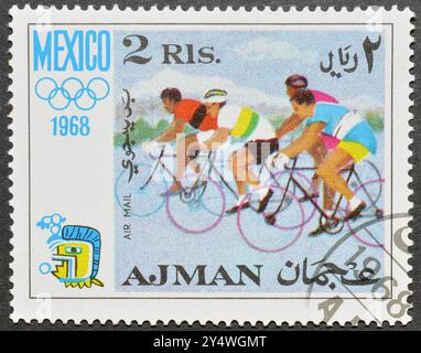 Gestempelte Briefmarke von Ajman, die Radfahren und Olympische Spiele in Mexiko zeigt, um 1968. Stockfoto