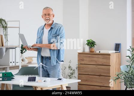 Ausgereifter Ingenieur mit Laptop- und Windturbinenmodellen auf dem Tisch im Büro Stockfoto