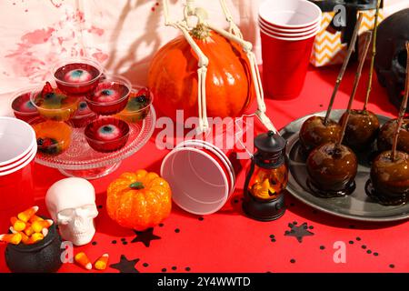 Süße Leckereien, Plastikbecher und Dekorationen für die Halloween-Party auf rotem Tisch Stockfoto