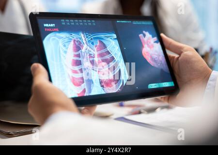 Ärzte und Krankenschwestern treffen sich, um die Lungenradiographie für die Patientenversorgungsstrategie in einem Behandlungszentrum zu diskutieren. Das medizinische Team analysiert Röntgenaufnahmen und Krankenakten von Organen, um sich auf die Diagnostik zu konzentrieren. Nahaufnahme. Stockfoto
