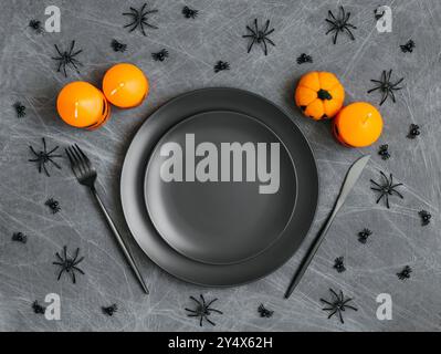 Halloween-Tisch mit schwarzem Geschirr, orangen Kerzen, Spinnweben und Spinnen auf grauem Hintergrund. Kopierbereich, Draufsicht, flache Ladefläche. Stockfoto