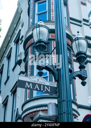 Hauptverkehrsschild an einem historischen Lampenträger mit einem historischen Gebäude im Hintergrund am Main Street Corridor in Downtown Houston, TX, USA. Stockfoto