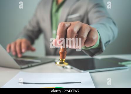 Geschäftsmann-Handstempel mit genehmigtem Stempel auf dem genehmigten Dokument am Schreibtisch, validiert und verwaltet Geschäftsdokumente und Vereinbarungen, Genehmigungsstatus Stockfoto