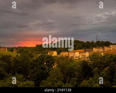 Ein atemberaubender Blick auf eine Vorstadtgemeinde, die im goldenen Licht einer untergehenden Sonne getaucht ist, mit Sturmwolken, die der Szene einen Hauch von Drama verleihen. Stockfoto