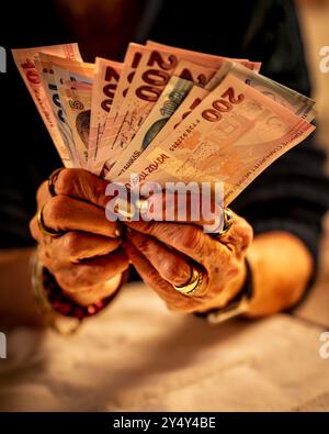 Eine ältere Frau, die mehrere türkische Lira-Banknoten hält, darunter 200 und 100 Lira-Banknoten. Ihre Hände sind mit Armbändern und Ringen verziert, und sie Stockfoto