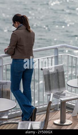 Eine junge Frau, die allein steht und sich auf Geländer stützt und in Tagträume blickt. Stockfoto