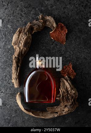 Flasche Brandy und alte Schlangen mit getrockneten Weinblättern auf schwarzem Steinhintergrund. Draufsicht. Stockfoto