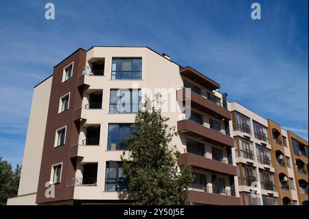 Ein elegantes, modernes Wohngebäude mit klaren Linien und einer Mischung aus braunen und cremefarbenen Fassaden. Große Fenster bieten viel Tageslicht in einem lebendigen Stockfoto