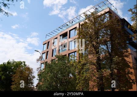 Modernes architektonisches Gebäude mit großen Fenstern und einer Dachterrasse vor klarem blauem Himmel in einer lebhaften städtischen Umgebung Stockfoto