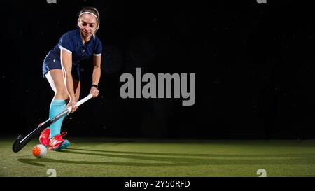 Eine entschlossene junge Frau, die den Ball geschickt mit dem Hockeyschläger anführt und sich auf ihr Spiel konzentriert. Isoliert auf schwarzem Hintergrund Stockfoto