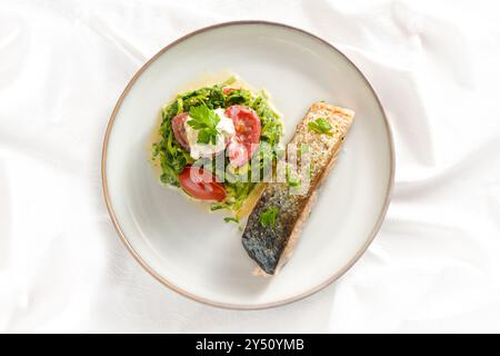 Lachs mit Haut gebraten, Gemüse aus Spinat und Tomaten mit Sahne und Petersilie garniert, gesundes Fischessen auf weißer Tischdecke, Hochwinkel V Stockfoto