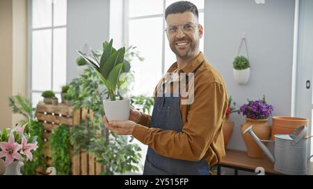 Ein lächelnder Mann hält Pflanze in einem sonnendurchfluteten Blumenladen, der ein Gefühl von Frische und Einzelhandel vermittelt. Stockfoto