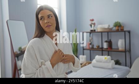 Junge Frau im weißen Bademantel im Spa, die einen Moment der Entspannung in einem Wellnesscenter mit minimalistischem Dekor genießt Stockfoto